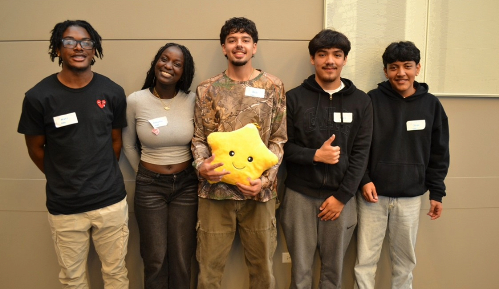 A group of five young individuals poses together, the middle student holding a stuffed yellow star toy.